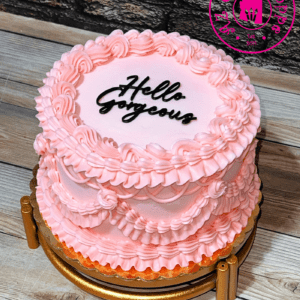 A pink frosted cake with 'Hello Gorgeous' written on top.